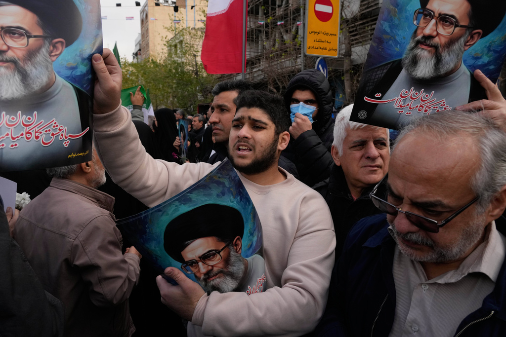 A man hands out posters of the Iranian Supreme Leader Ayatollah Ali Khamenei during a funeral ceremony for a group of security forces, who were killed during anti-government protests, in Tehran, Iran, Wednesday, Jan. 14, 2026. (AP Photo/Vahid Salemi)