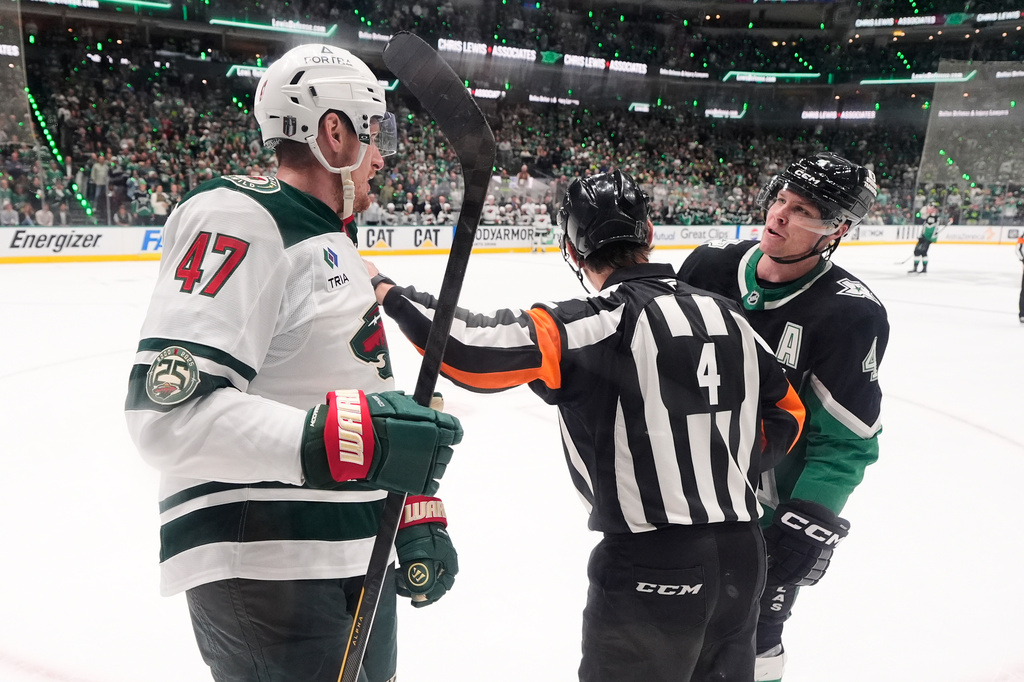 Minnesota Wild's Michael McCarron (47) and Dallas Stars' Miro Heiskanen (4) exchange words as referee Wes McCauley (4) stands between them in the second period of Game 2 of a first-round NHL Stanley Cup playoffs hockey series Monday, April 20, 2026, in Dallas. (AP Photo/Tony Gutierrez)un