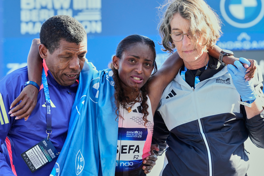 Ethiopia's Tigist Assefa is lead away by former runner Haile Gebrselassie, left, and a medical after winning the Berlin Marathon in Berlin, Germany, Sunday, Sept. 27, 2026. (AP Photo/Ebrahim Noroozi)