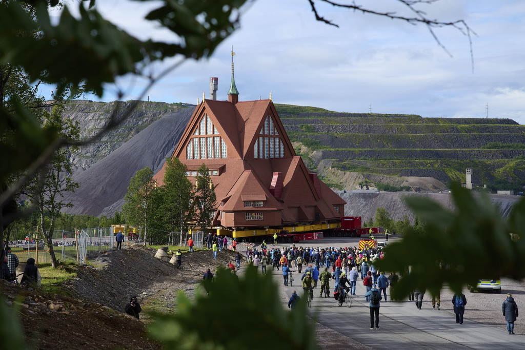 People gather outside the Kiruna Church, a Sami style wooden Swedish Lutheran church, called Kiruna Kyrka in Swedish, in Kiruna, Sweden, Tuesday, Aug. 19, 2025, during its move along a 5-kilometer (3-mile) route east to a new city center as part of the town's relocation. (AP Photo/Malin Haarala)