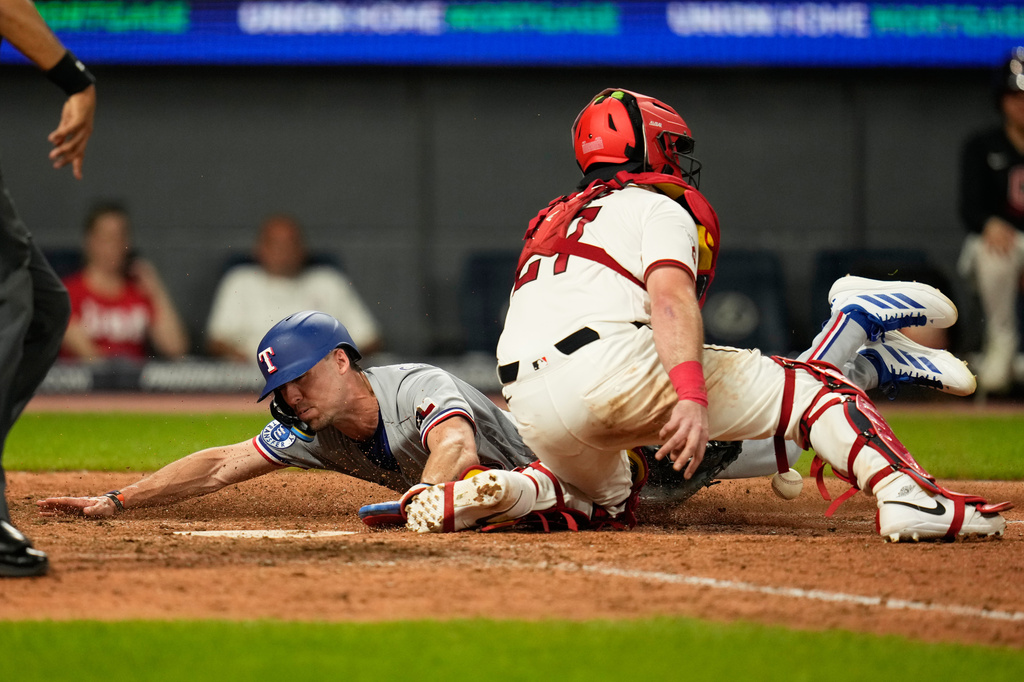 Texas Rangers' Evan Carter, left, scores behind Cleveland Guardians catcher Austin Hedges (27) in the ninth inning of a baseball game in Cleveland, Monday, June 29, 2026. (AP Photo/Sue Ogrocki)