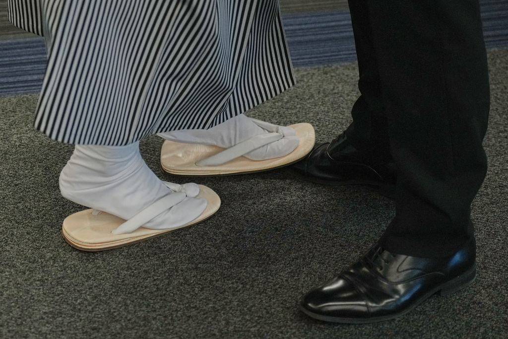 Two young men stand side by side, one wearing traditional zori sandals and tabi socks and the other in dress shoes, chat before celebrating the Coming-of-Age Day, a centuries-old tradition and national holiday making the milestone from childhood to adulthood, Monday, Jan. 12, 2026, in Yokohama near Tokyo. (AP Photo/Eugene Hoshiko)