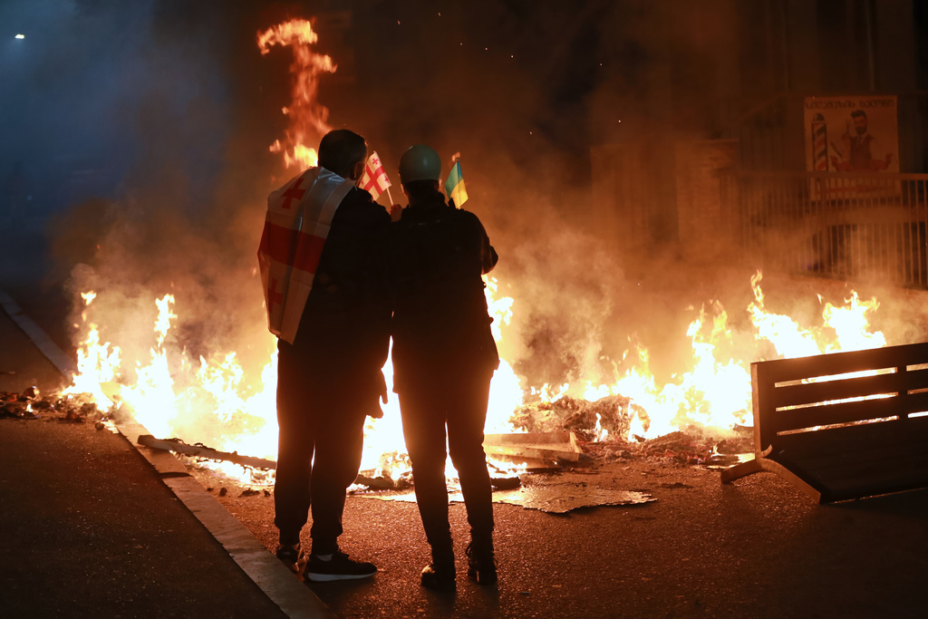 Demonstrators with a Georgian and Ukrainian national flags stand behind a burning barricade not far from a police line during an opposition rally in the city center of Tbilisi, Georgia, on Saturday, Oct. 4, 2025, boycotting the municipal elections and calling for the release of political opponents. (AP Photo/Zurab Tsertsvadze)