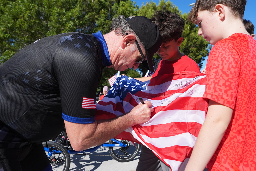 Wounded Warriors Project CEO Walt Piatt, left, signs an American flag for students outside of the Coral Shores High School as wounded veterans ride in the annual Florida Keys Soldier Ride organized by the Wounded Warrior Project, Friday, Jan. 9, 2026, in Islamorada, Fla. (AP Photo/Lynne Sladky)