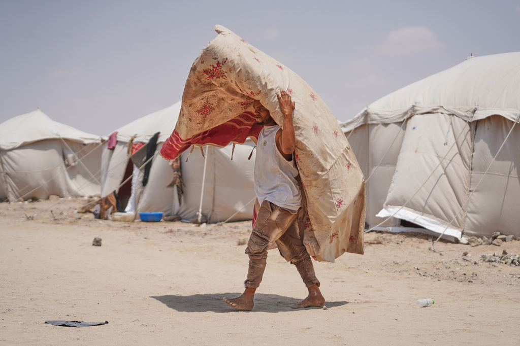 A displaced Yemeni carries a carpet at Al-Firdaws camp in Ras Imran, just outside Aden, Yemen, Monday, Sept. 14, 2026. (AP Photo/Abdulnasser Alseddik)