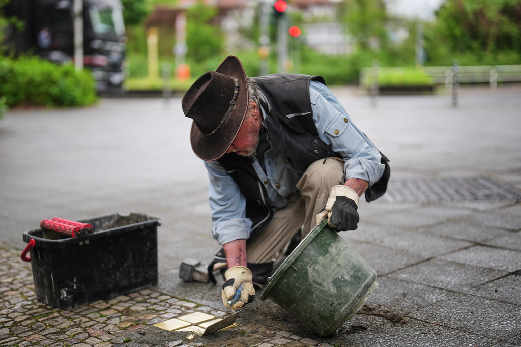 FILE - Artist Gunter Demnig places a palm-sized brass Holocaust plaques called, "Stolpersteine," or "Stumbling Blocks," with the names of victims of the Nazi regime in front of their former home at a street in Berlin, Germany, May 6, 2026. (AP Photo/Markus Schreiber, File)