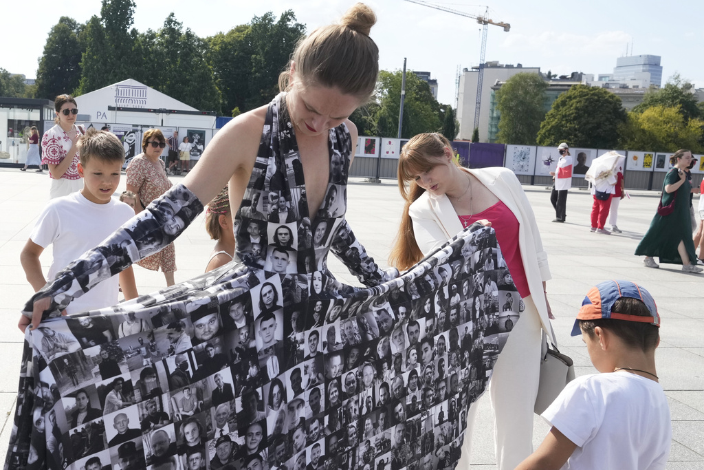 Antanina Kanavalava, center right, a former political prisoner in Belarus, looks at photos of other prisoners printed on a dress at the Freedom March for Belarus in Warsaw, Poland, on Saturday, Aug. 9, 2025. (AP Photo/Czarek Sokolowski)