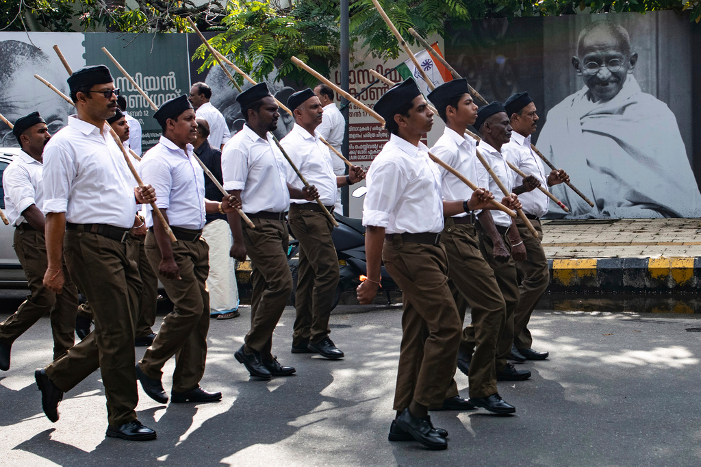 FILE - Rashtriya Swayamsevak Sangh (RSS) volunteers march through a street in Kochi, Kerala, India, Sunday, Oct. 13, 2024, in front of a poster of Mahatma Gandhi displayed as part of celebrations marking 100th year of Gandhi assuming office as the Indian National Congress party president. (AP Photo/R S Iyer, File)