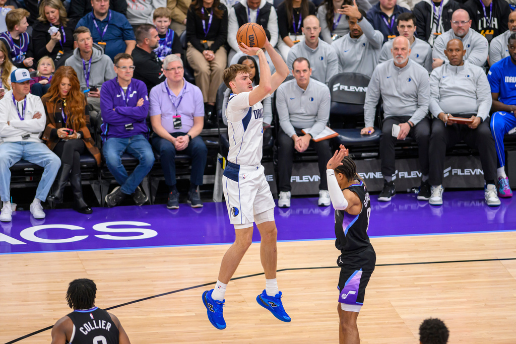 Dallas Mavericks forward Cooper Flagg, center, shoots over Utah Jazz guard Keyonte George, right, during the first half of an NBA basketball game, Monday, Dec. 15, 2025, in Salt Lake City. (AP Photo/Tyler Tate)