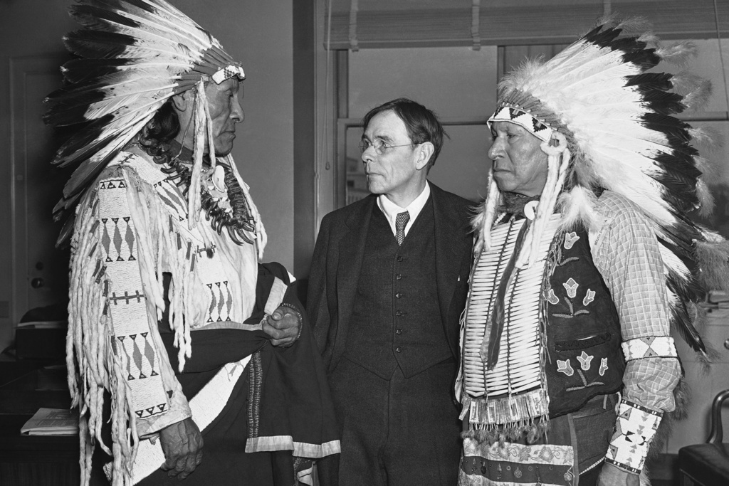 FILE - In full tribal regalia, Dewey Beard, left, and James Pipe-on-Head, survivors of the Wounded Knee massacre of 1890 in South Dakota, arrived in Washington on March 4, 1938, to testify in behalf of a bill to pay survivors of the event in which hundreds of Lakota people were killed by U.S. soldiers. They are greeted by John Collier, center, Commissioner of Indian Affairs. (AP Photo, File)