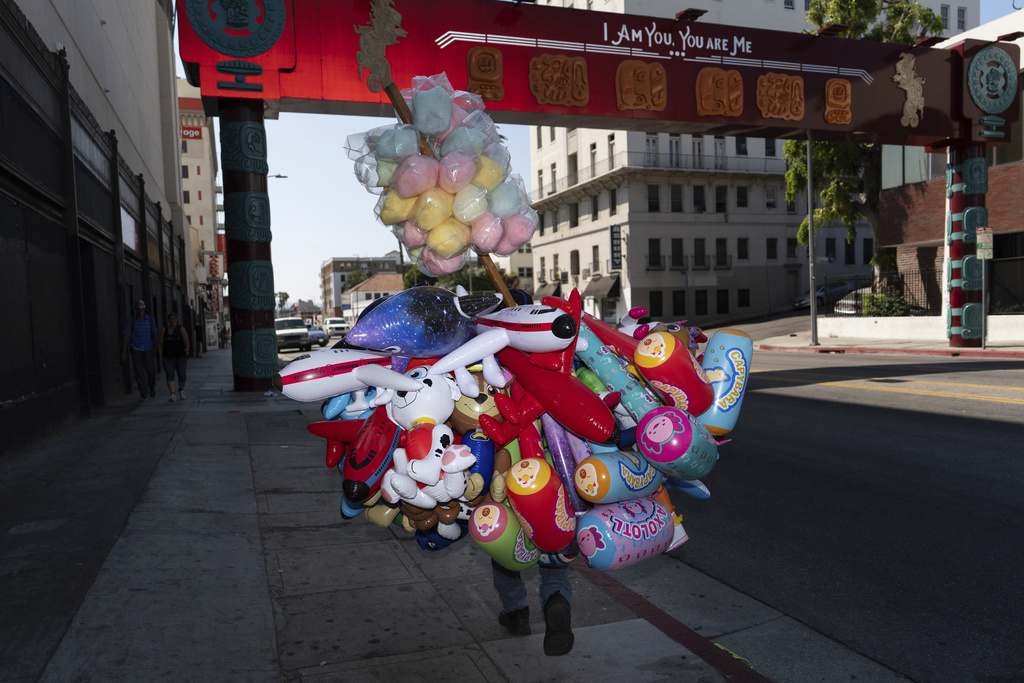 A street vendor carries cotton candy and inflatable toys near MacArthur Park in Los Angeles, an area targeted in recent ICE raids, Saturday, July 19, 2025. (AP Photo/Jae C. Hong)