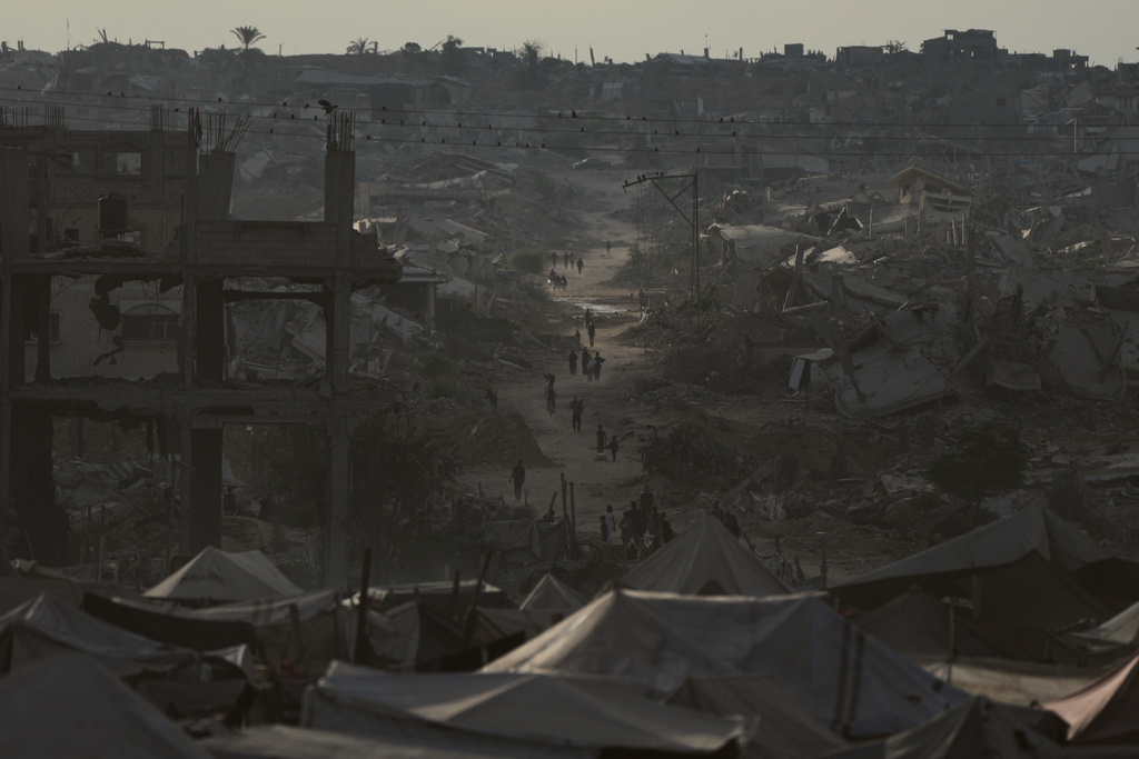 Displaced Palestinians walk trough destroyed homes and buildings in Khan Younis, Gaza Strip, Saturday, Oct. 18, 2025. (AP Photo/Jehad Alshrafi)