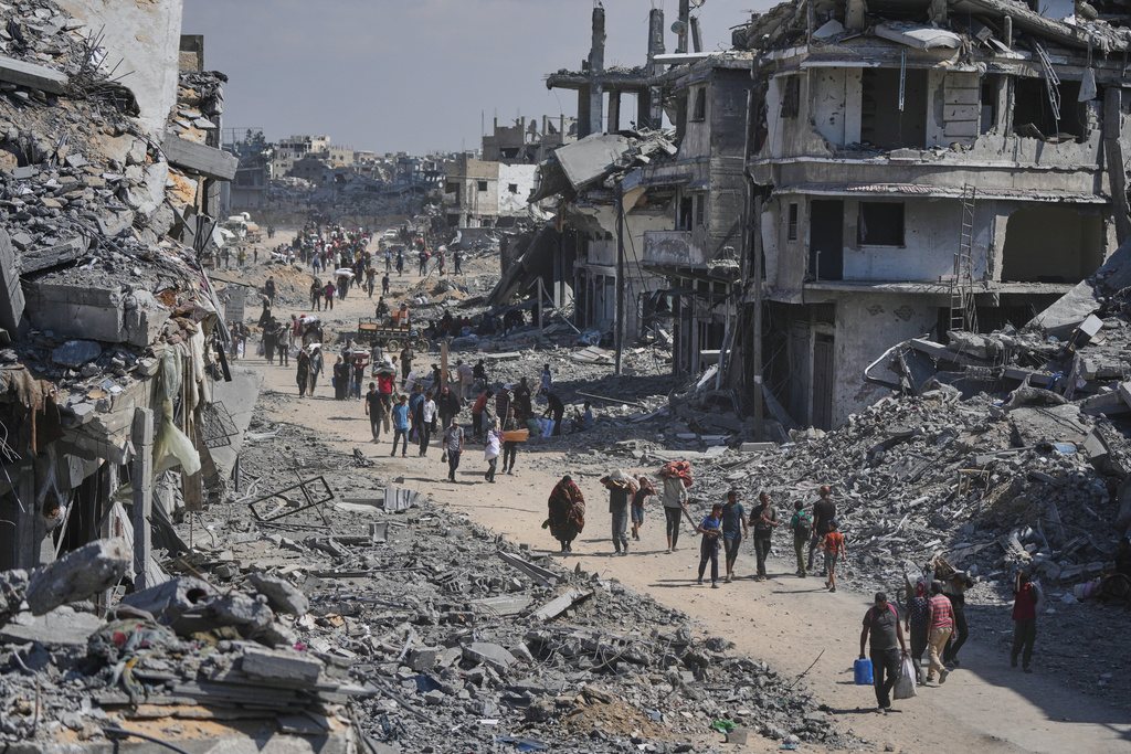 Displaced Palestinians walk with their belongings past destroyed buildings as they return to their homes in Khan Younis, southern Gaza Strip, Friday, Oct. 10, 2025, after Israel and Hamas agreed to a pause in their war and the release of the remaining hostages. (AP Photo/Jehad Alshrafi)