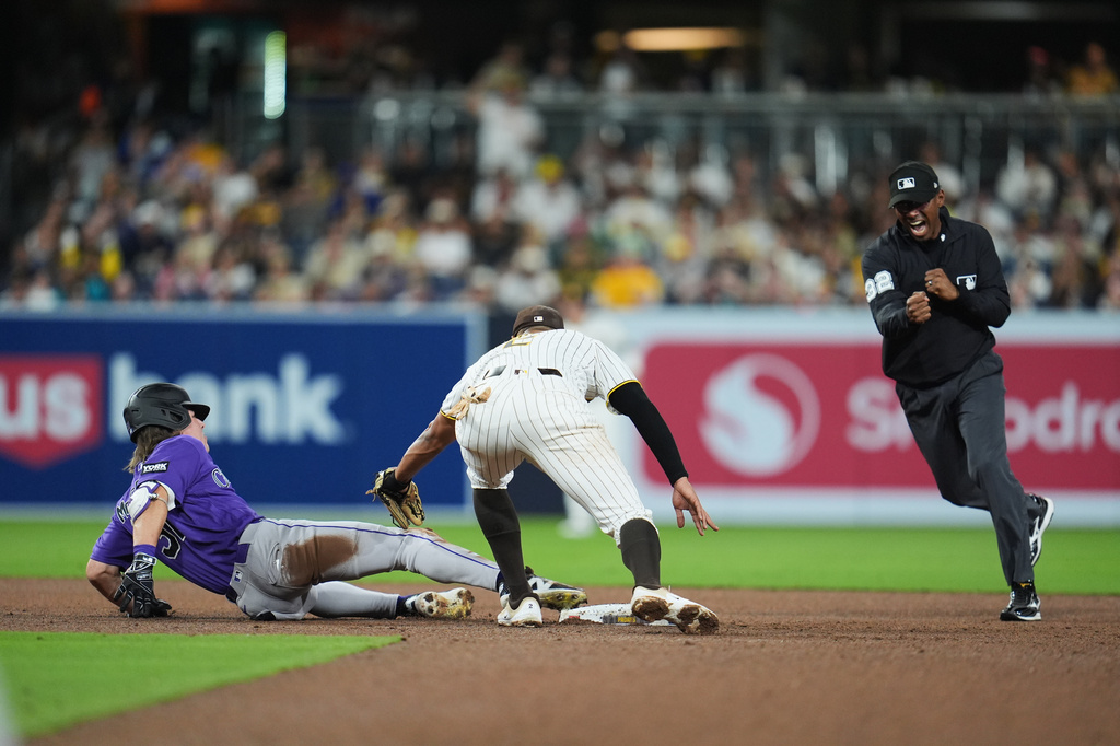 Colorado Rockies' Jake McCarthy, left, is tagged out by San Diego Padres shortstop Xander Bogaerts after trying to advance to second off a single as umpire Edwin Moscoso makes the call, right, during the fifth inning of a baseball game Thursday, April 9, 2026, in San Diego. (AP Photo/Gregory Bull)