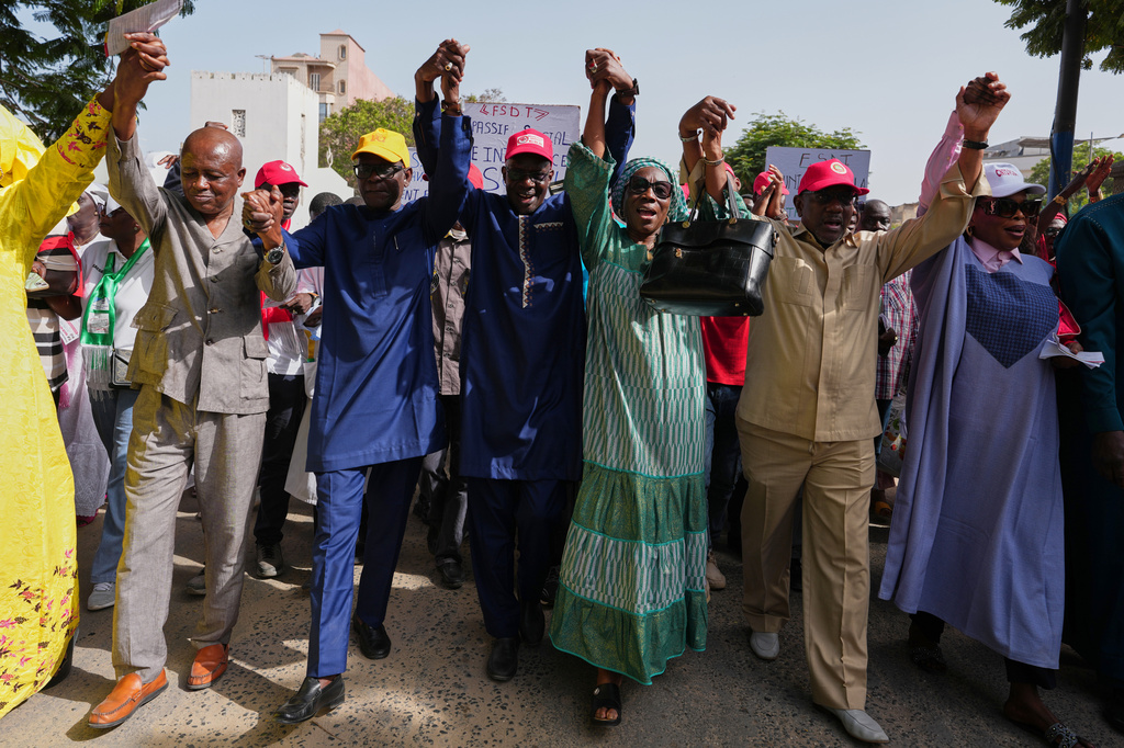 Workers hold hands as they march to demand that the government honor its commitments and address their concerns, in Dakar, Senegal, Wednesday, April 8, 2026. (AP Photo/Misper Apawu)