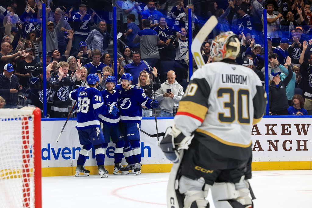 Tampa Bay Lightning's Nikita Kucherov, center back left, celebrates after his winning goal against Vegas Golden Knights' Carl Lindbom (30) with teammates Brandon Hagel (38) and J.J. Moser (90) during the overtime period of an NHL hockey game Sunday, Oct. 26, 2025, in Tampa, Fla. (AP Photo/Mike Carlson)