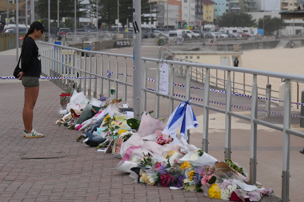 FILE - A woman stands at a flower tribute at Bondi Beach on Dec. 16, 2025, following Sunday's shooting in Sydney, Australia. (AP Photo/Mark Baker, File)