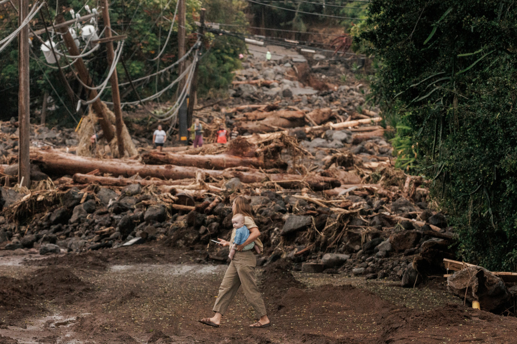 A woman and child walk past a debris-strewn street in Naalehu, Hawaii, Monday, Aug. 17, 2026, after a severe weather system went through the area. (Stephen Lam/San Francisco Chronicle via AP)