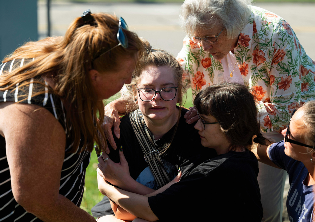 Joanne Green of Fenton, 75, top right, and McKenna Harrington of Davison, 25, second from right, comfort Katelyn Kruse of Fenton, 26, center, after Kruse was present at the scene of a shooting and structure fire at The Church of Jesus Christ of Latter-day Saints on McCandlish Road in Grand Blanc, Mich., Sunday, Sept. 28, 2025. (Katy Kildee/Detroit News via AP)