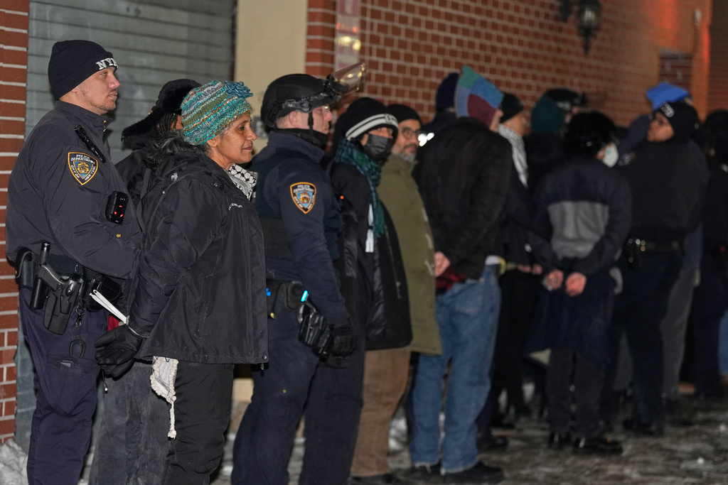 Protesters in cuffs wait to be loaded into a bus after staging a sit-in at the lobby of a Hilton Garden Inn in New York, Tuesday, Jan. 27, 2026. (AP Photo/Seth Wenig)