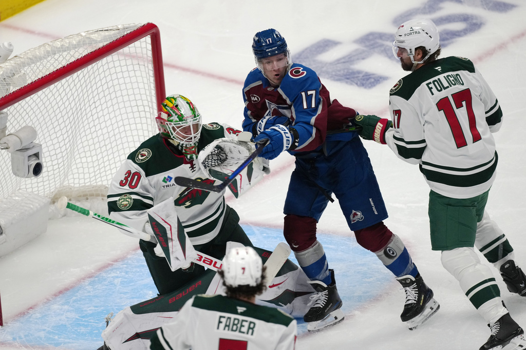 Colorado Avalanche center Parker Kelly, center top, tries to redirect a shot at Minnesota Wild goaltender Jesper Wallstedt (30) as Wild left wing Marcus Foligno, right, covers in the first period of Game 1 of an NHL hockey Stanley Cup second-round playoff series Sunday, May 3, 2026, in Denver. (AP Photo/David Zalubowski)