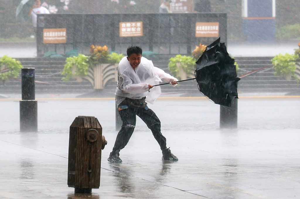 In this photo released by Xinhua News Agency, a man fights to hold onto to his umbrella in strong wind and rain ahead of Typhoon Dolphin at Huangpu District of Shanghai, China, Sunday, Aug. 9, 2026. (Wang Xiang/Xinhua via AP)