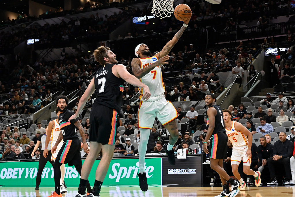 Atlanta Hawks guard Nickeil Alexander-Walker, center, goes to the basket against San Antonio Spurs center Luke Kornet during the first half of an NBA basketball game, Thursday, Nov. 20, 2025, in San Antonio. (AP Photo/Darren Abate)