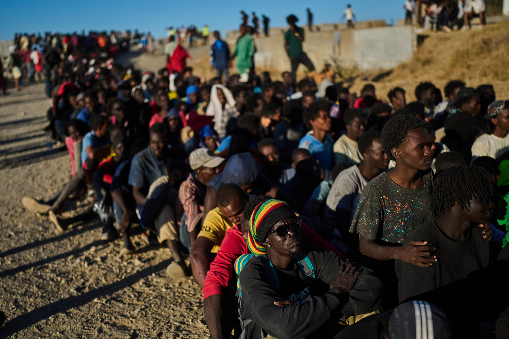 Migrants who crossed from Morocco into Spain line up for food distribution on a beach in the Spanish enclave of Ceuta, Monday, Aug. 3, 2026. (AP Photo/Bernat Armangue)