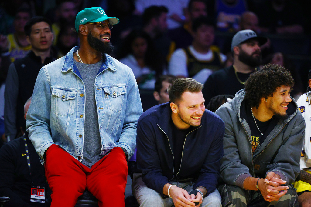 Los Angeles Lakers forward LeBron James (23) and Los Angeles Lakers guard Luka Doncic (77) watch from the bench during the second half of an NBA basketball game against the Portland Trail Blazers, Monday, Oct. 27, 2025, in Los Angeles. (AP Photo/Ethan Swope)