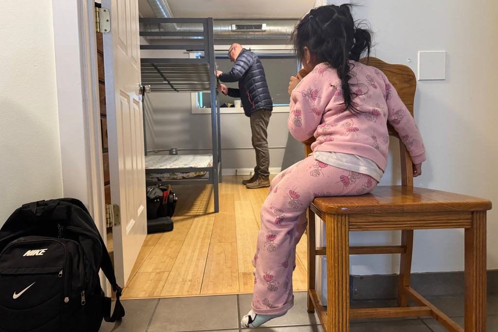 A child whose family is being sought by federal immigration agents watches as a volunteer prepares a bunk bed for her family at a Minneapolis safe house Friday, Jan. 16, 2026. (AP Photo/Jack Brook)