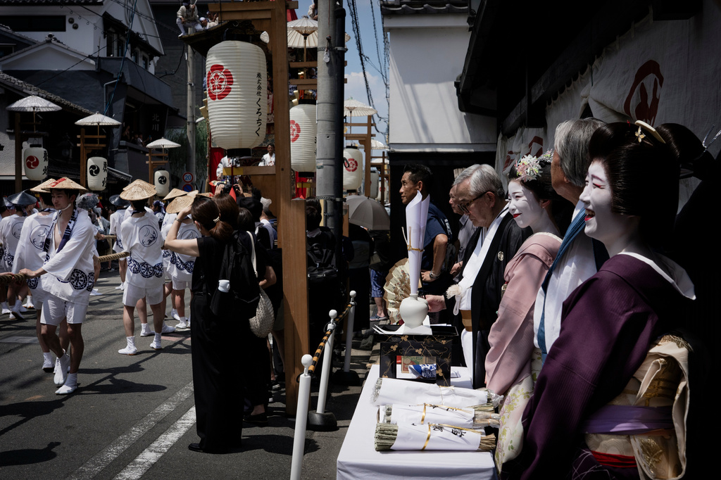 A geiko, a regional word for geisha, and a maiko watch festivalgoers pass by during one of the main parades of Shinto's Gion Matsuri festival in Kyoto, western Japan, Friday, July 17, 2026. (AP Photo/Fred Mery)