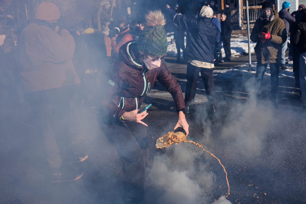 A protester grabs a tear gas grenade deployed by federal immigration officers near the scene where Renee Good was fatally shot by an ICE officer last week, Tuesday, Jan. 13, 2026, in Minneapolis. (AP Photo/John Locher)