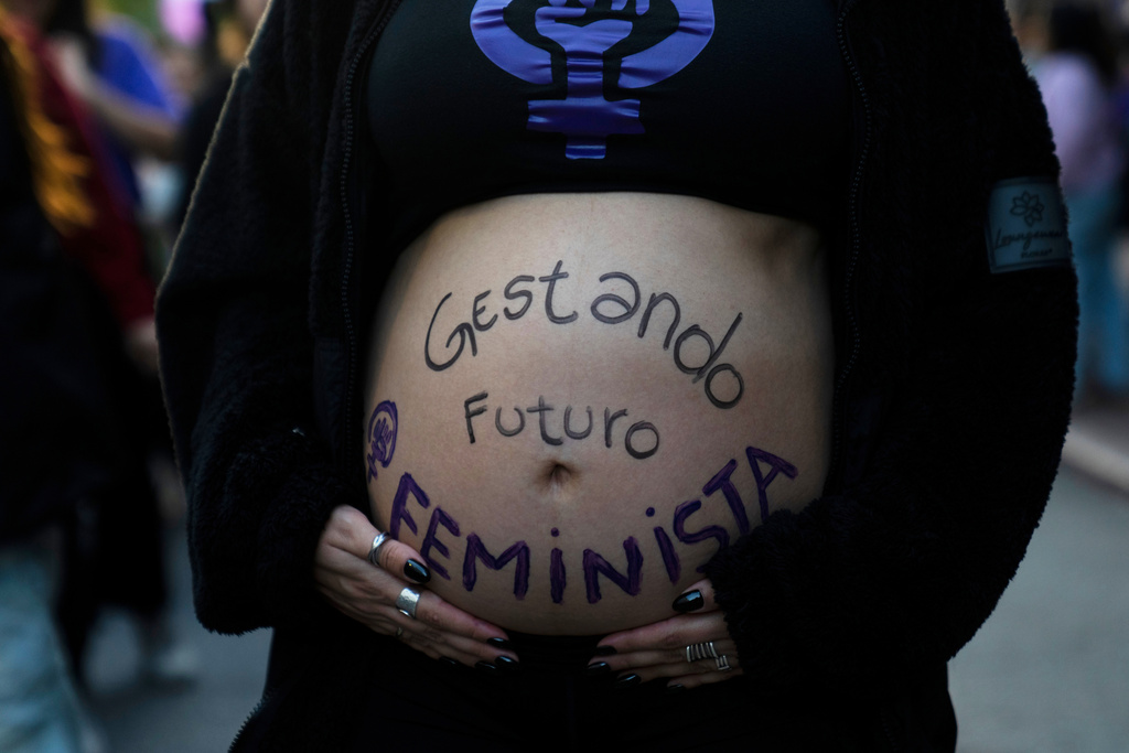 A pregnant woman bears the phrase "Gestating a feminist future" in Spanish on her stomach during a rally marking International Women's Day in downtown Montevideo, Uruguay, Sunday, March 8, 2026. (AP Photo/Matilde Campodonico)