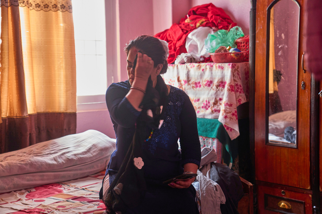 A 54-year-old mother of a Nepali migrant checks her phone at home in Kathmandu, Nepal, on Tuesday, May 19, 2026, before calling her son to find out whether he has arrived safely in Abu Dhabi, as she sits on his bed. (AP Photo/Niranjan Shrestha) CORRECTION removes name of mother and changes to 54-year-old mother of Nepali migrant