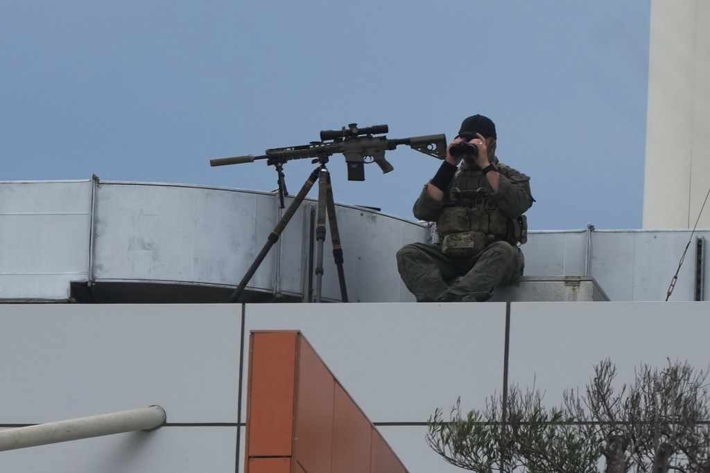 A masked man with the authorities sits with a firearm on the roof of a building at Bondi Beach in Sydney, Sunday, Dec. 21, 2025, ahead of a ceremony to mark the National Day of Reflection for victims and survivors from the Bondi shooting on Dec. 14. (AP Photo/Mark Baker)
