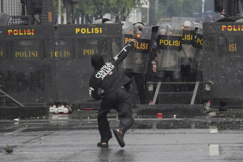 Police officers cover themselves with riot shields as a protester throws rock at them during a protest against lavish allowances given to parliament members, outside the parliament in Jakarta, Indonesia, Sunday, Aug. 31, 2025. (AP Photo/Dita Alangkara)