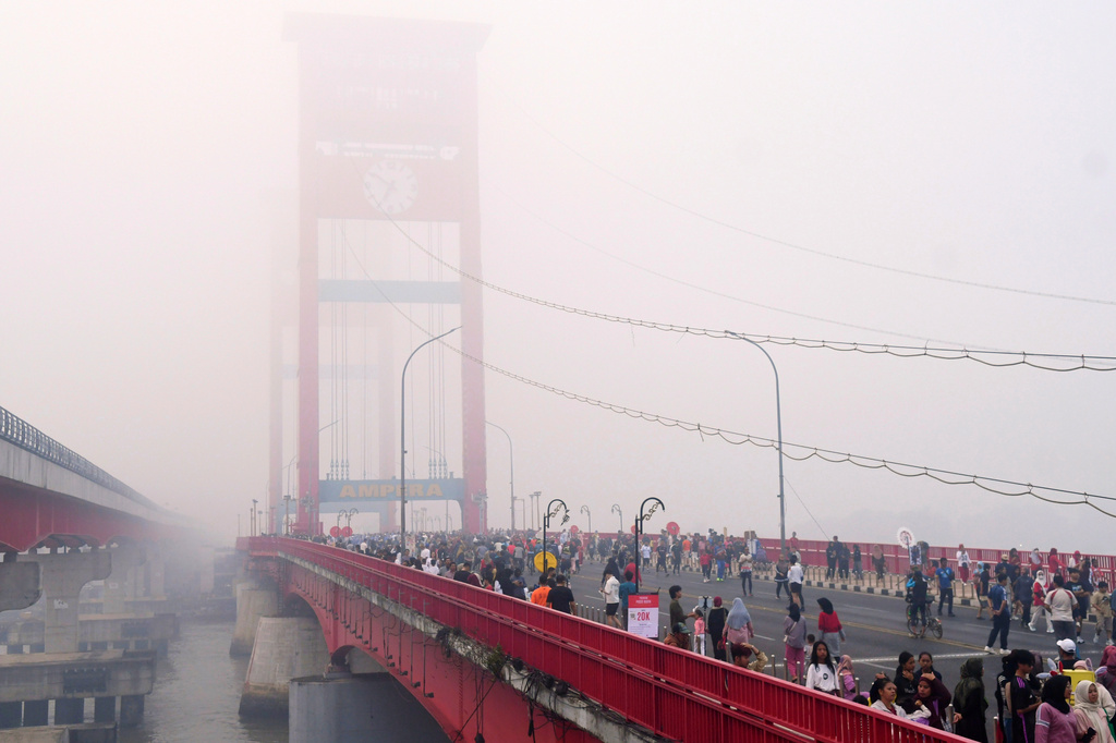 People walk along the Ampera Bridge as haze from wildfires blankets the city of Palembang, in South Sumatra, Indonesia, Sunday, Aug. 23, 2026. (AP Photo/Muhammad Fajri)