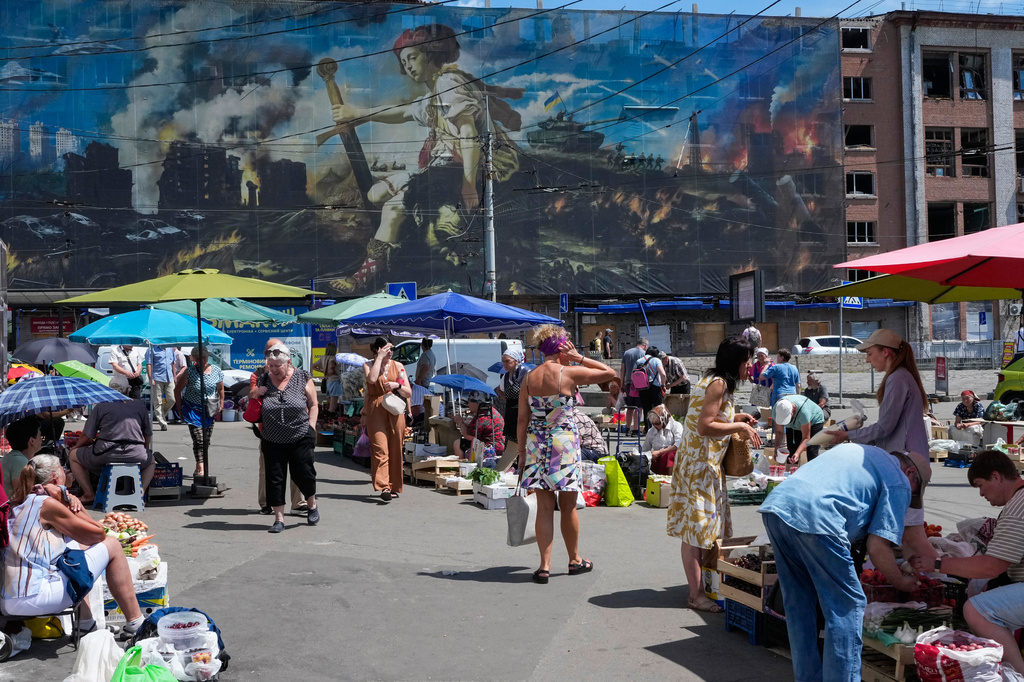 People buy food at an improvised outdoor market surrounded by damaged buildings covered with street artist paintings close to a big city marketplace that was ruined recently by Russian missiles in Kyiv, Ukraine, Monday, June 22, 2026. (AP Photo/Efrem Lukatsky)