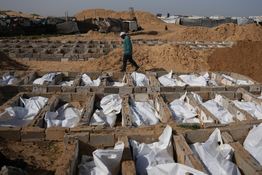 A man walks past graves containing the bodies of unidentified Palestinians returned from Israel as part of the ceasefire deal during their burial in Deir al-Balah, Gaza Strip, Friday, Feb. 13, 2026. (AP Photo/Abdel Kareem Hana)