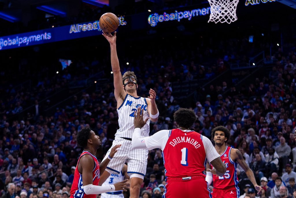 Orlando Magic's Franz Wagner, top, shoots the ball over Philadelphia 76ers' Justin Edwards, left, and Andre Drummond (1) during the first half of an NBA Cup basketball game, Tuesday, Nov. 25, 2025, in Philadelphia. (AP Photo/Chris Szagola)