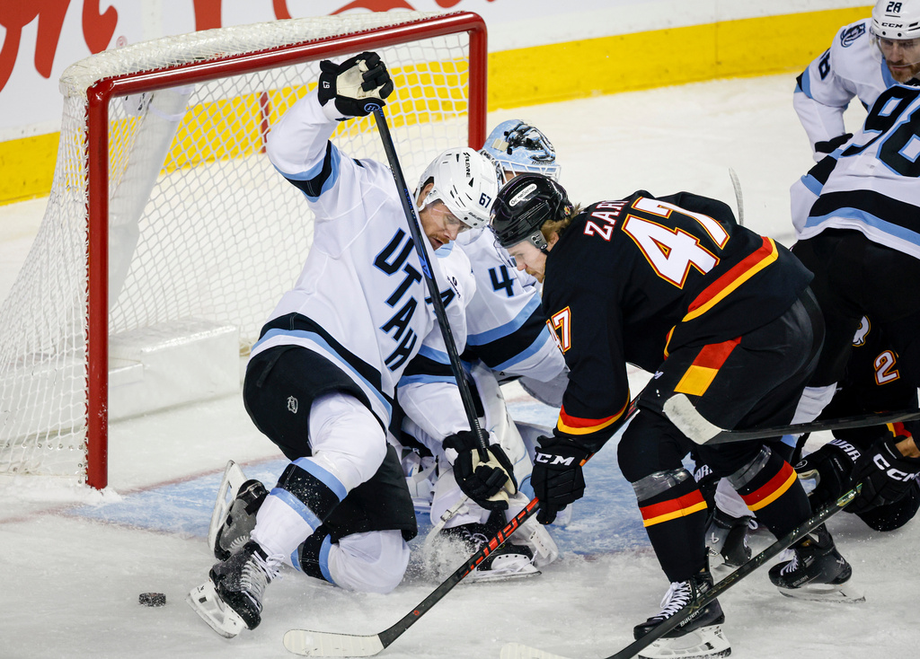 Utah Mammoth's Lawson Crouse, left, tries to get the puck away from Calgary Flames' Connor Zary (47) during first-period NHL hockey game action in Calgary, Alberta, Saturday, Dec. 6, 2025. (Jeff McIntosh/The Canadian Press via AP)