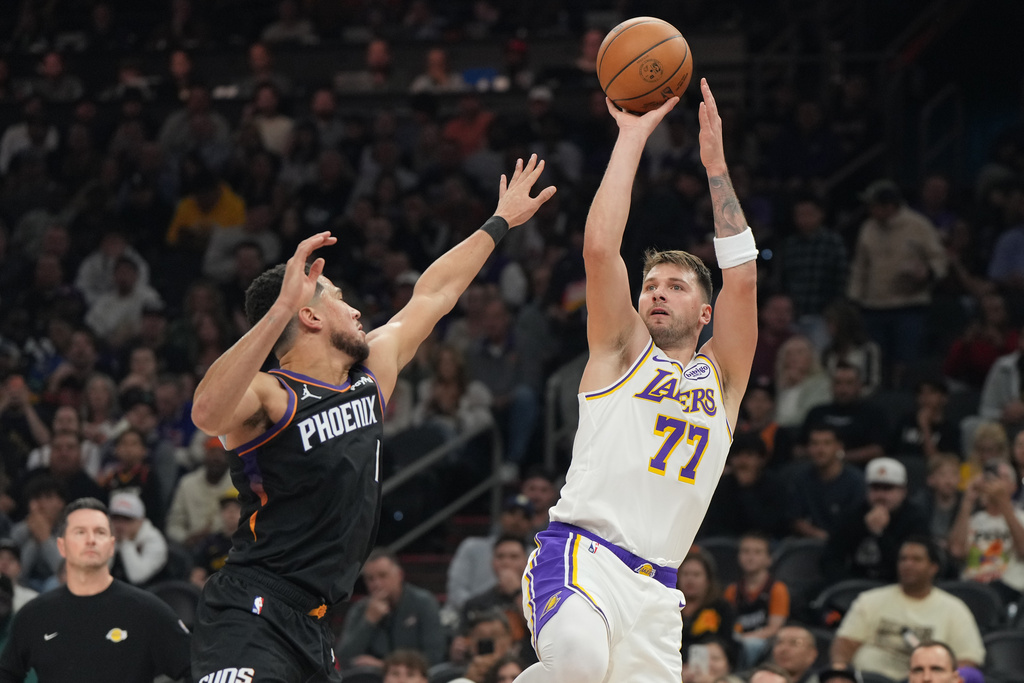 Los Angeles Lakers guard Luka Doncic (77)looks to shoot over Phoenix Suns guard Devin Booker, front left, during the first half of an NBA basketball game, Sunday, Dec. 14, 2025, in Phoenix. (AP Photo/Rick Scuteri)