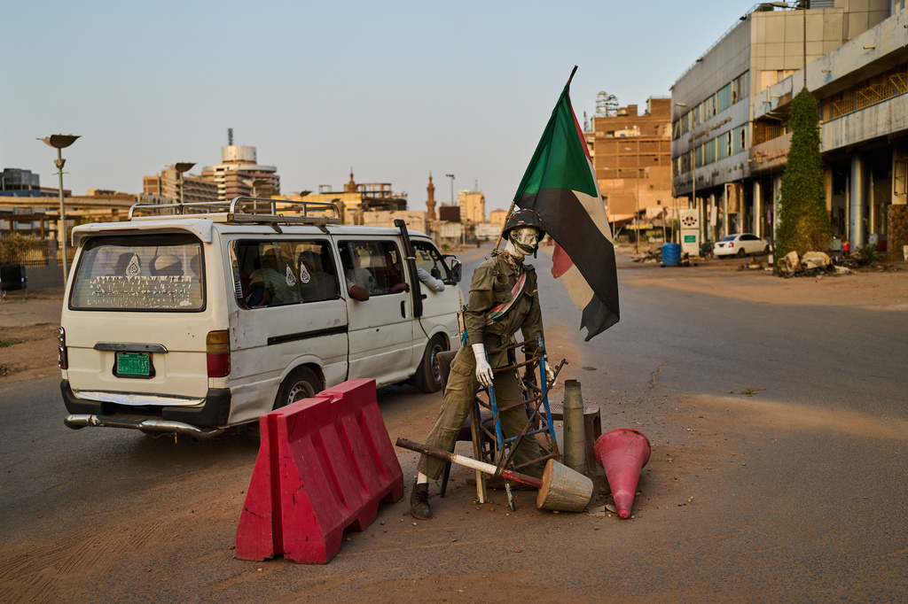 A minibus drives past an empty checkpoint where a mannequin dressed as a soldier stands in downtown Khartoum, Sudan, Sunday, April 19, 2026. (AP Photo/Bernat Armangue)