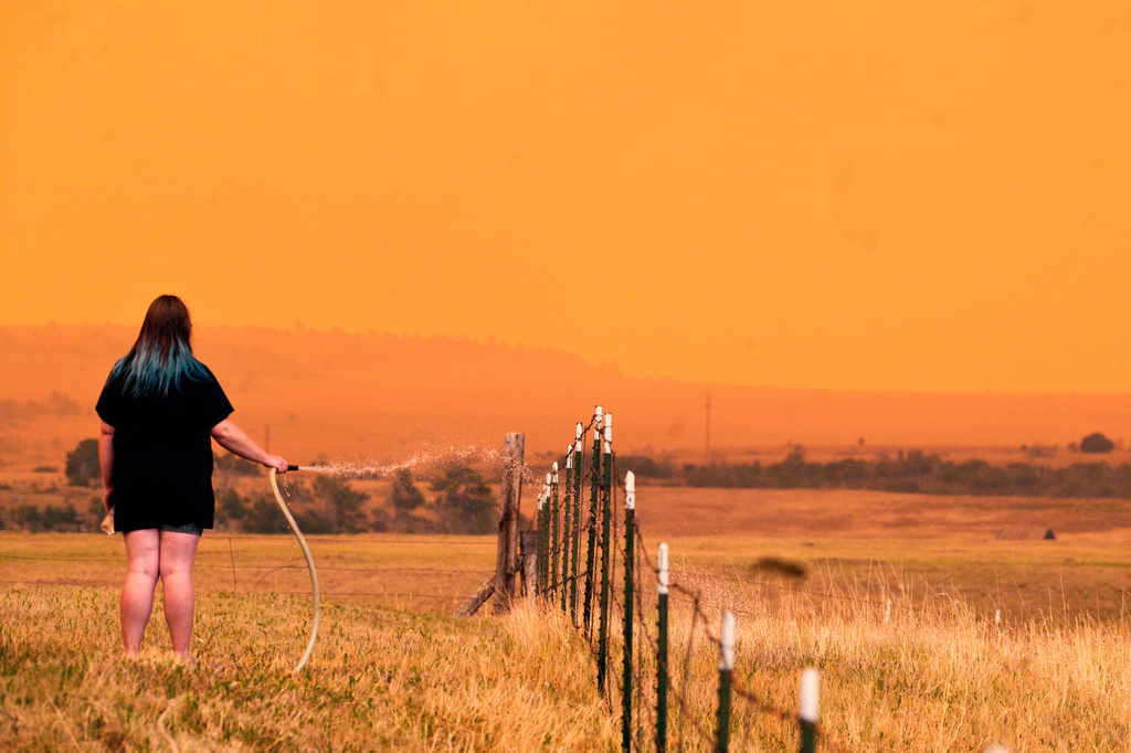 A woman uses a hose to wet down grass around the Mountain Shadows Mobile Estates in hopes of keeping the Aspen Acres fire from reaching homes in the mobile home park near Beulah, Colo., on Monday, June 29, 2026. (Jerilee Bennett/The Gazette via AP)