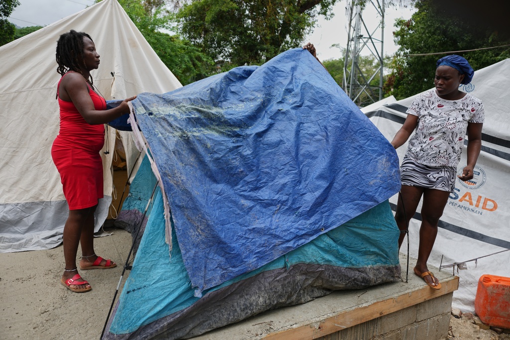 People place plastic tarps over their tents ahead of expected rain at a shelter for families displaced by gang violence in Port-au-Prince, Haiti, Thursday, Oct. 23, 2025. (AP Photo/Odelyn Joseph)