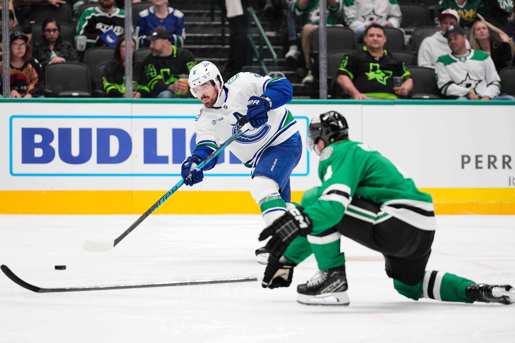 Vancouver Canucks right wing Conor Garland (8) takes a shot as Dallas Stars defenseman Miro Heiskanen (4) defends in the second period of an NHL hockey game Thursday, Oct. 16, 2025, in Dallas. (AP Photo/Tony Gutierrez)