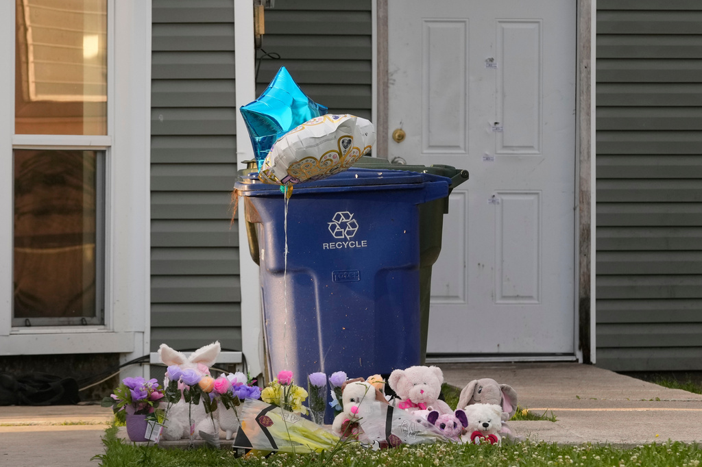 A makeshift memorial is growing on the front lawn of a home as the door in the background shows bullet holes and evidence markers where children were killed during a mass shooting the day before in Shreveport, La., Monday, April 20, 2026. (AP Photo/Gerald Herbert)