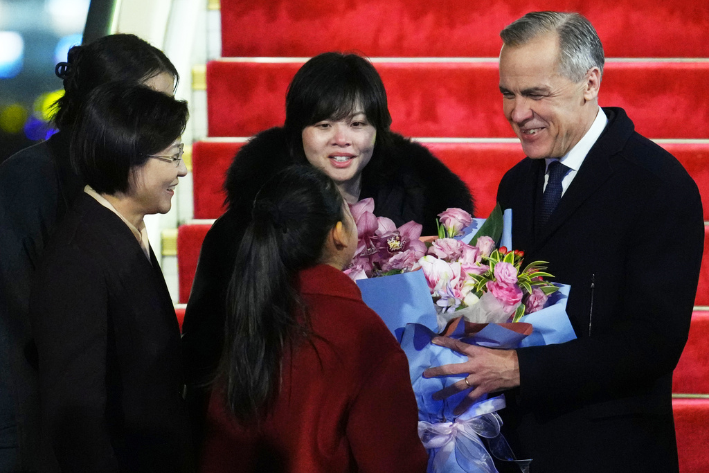 Canada's Prime Minister Mark Carney is presented with flowers from Lu You Ci, 11, during his welcome ceremony after deplaing in Beijing, China, Wednesday, Jan. 14, 2026. (The Canadian Press/Sean Kilpatrick, via AP)