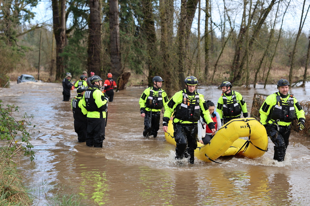 In this photo provided by Clackamas Fire District, rescuers use an inflatable raft to save a family whose car was trapped in floodwaters on a roadway in Molalla, Ore., Friday, Dec. 19, 2025. (Clackamas Fire District via AP)