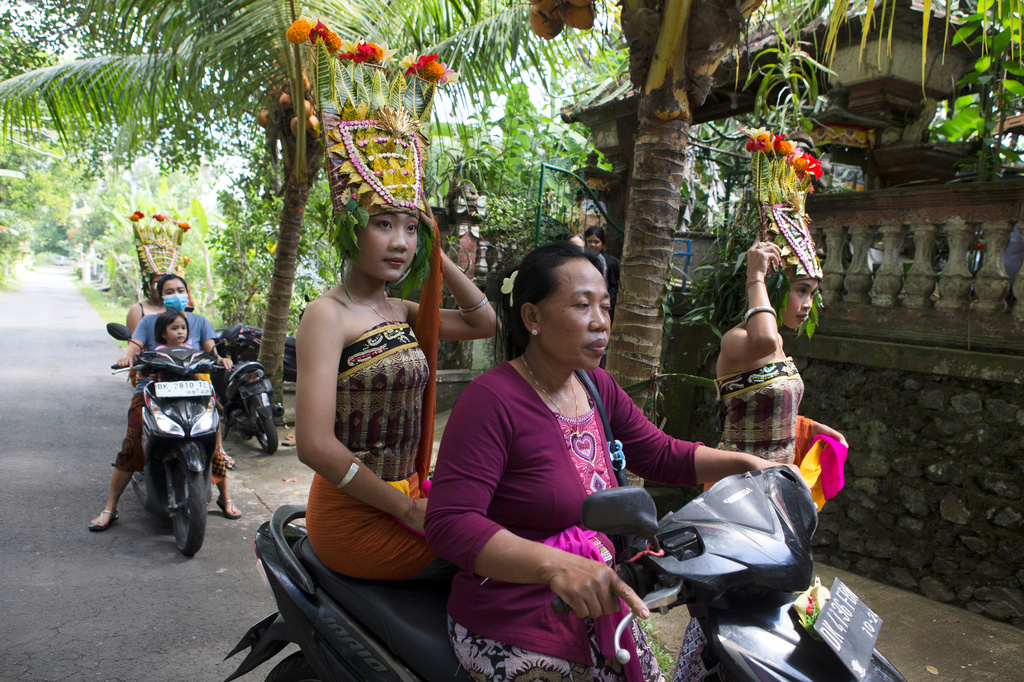Ketut Alit Widiantary hops on a motorbike before performing the sacred Rejang dance during Kuningan holiday, which marks the end of the 10-day Galungan festival celebrating the victory of good over evil, in Karangasem, Bali, Indonesia, Saturday, June 27, 2026. (AP Photo/Firdia Lisnawati)